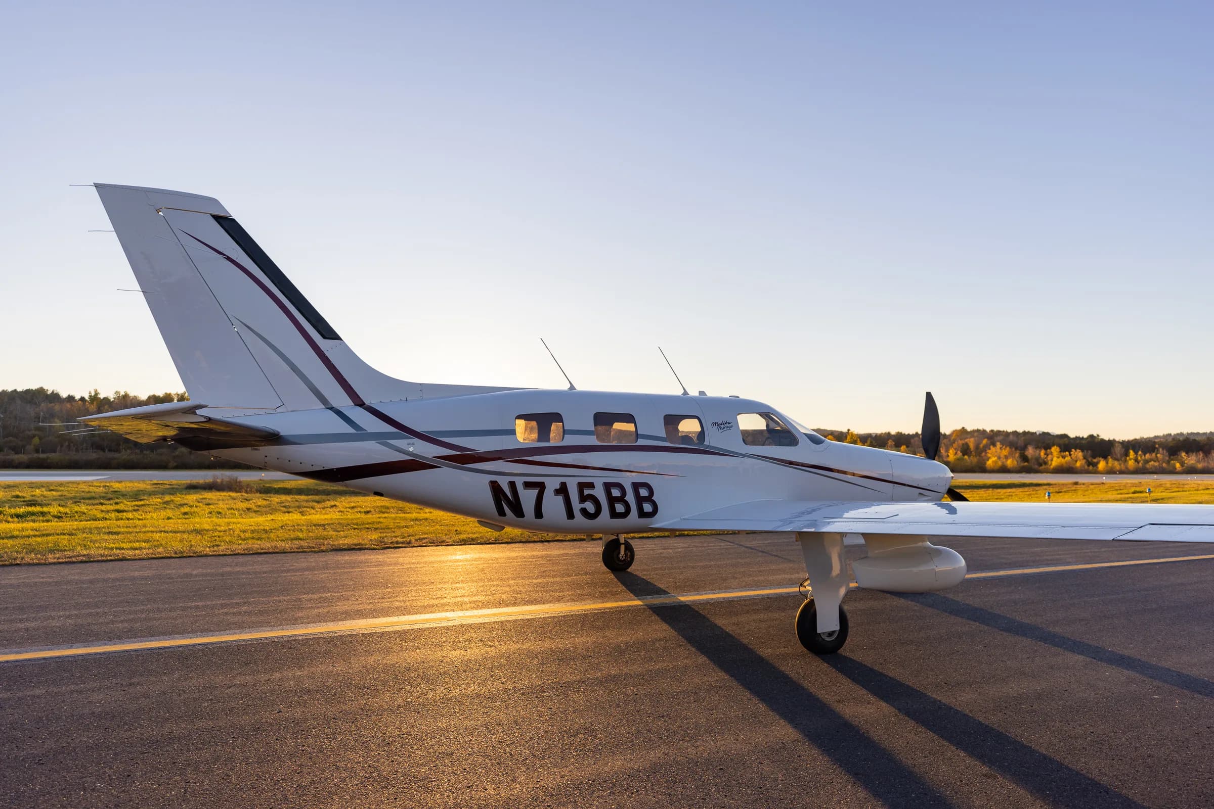 A side view of the Piper Malibu Mirage N715BB with its wing extended on a runway at sunset.