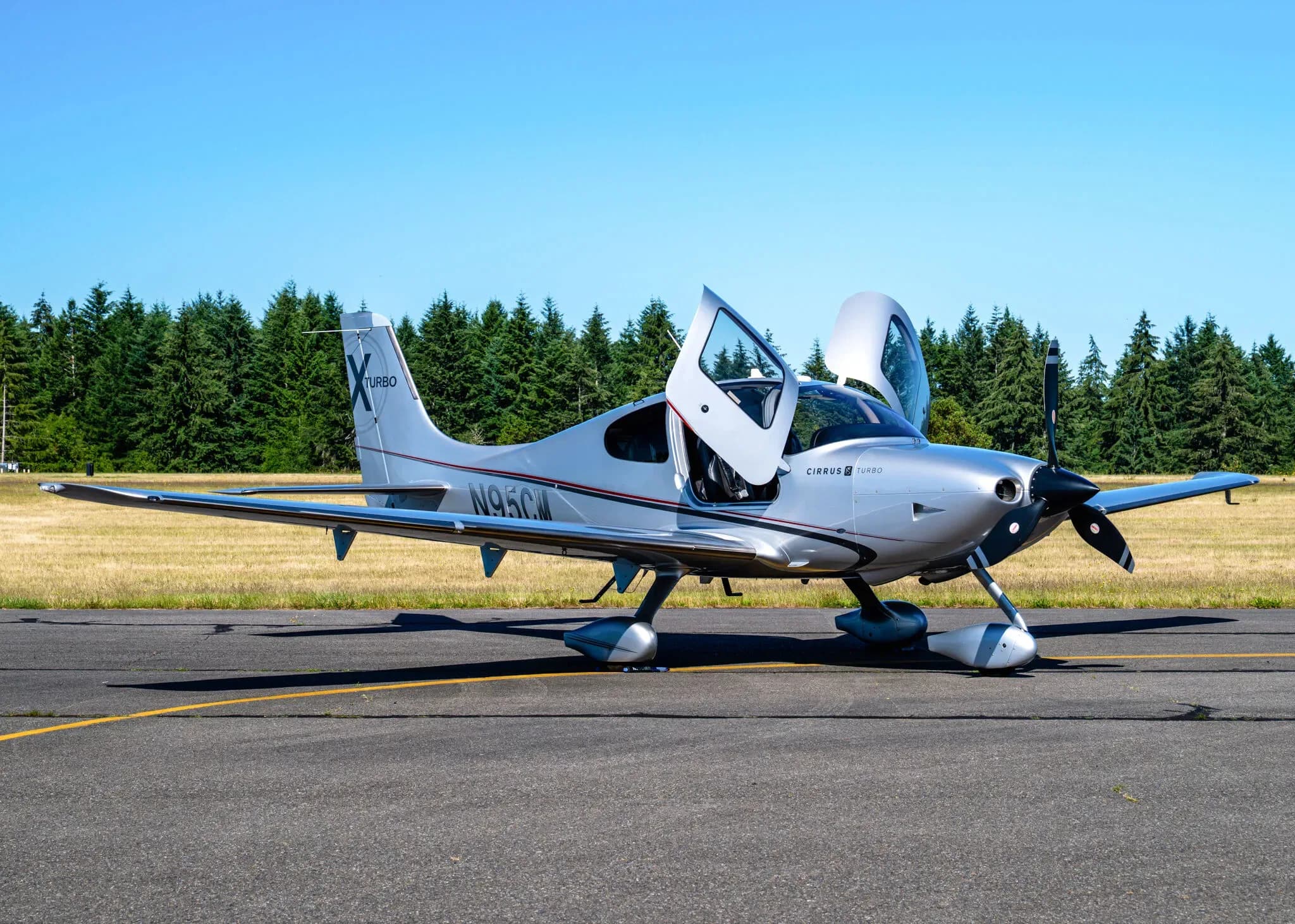 A silver Cirrus SR22T aircraft with registration N95CM parked on an airfield with its gull-wing doors open.