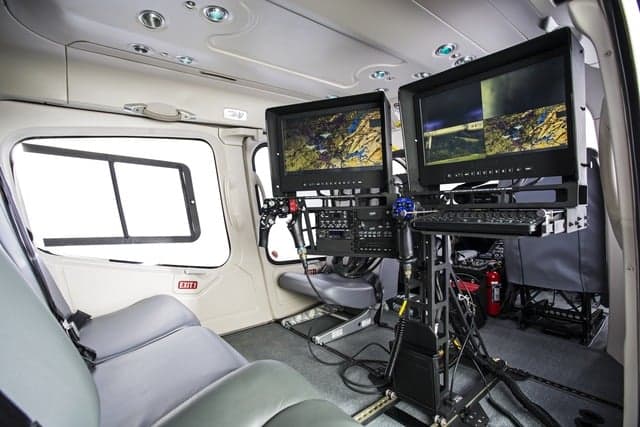 Interior view of a helicopter with two large monitors and seats.