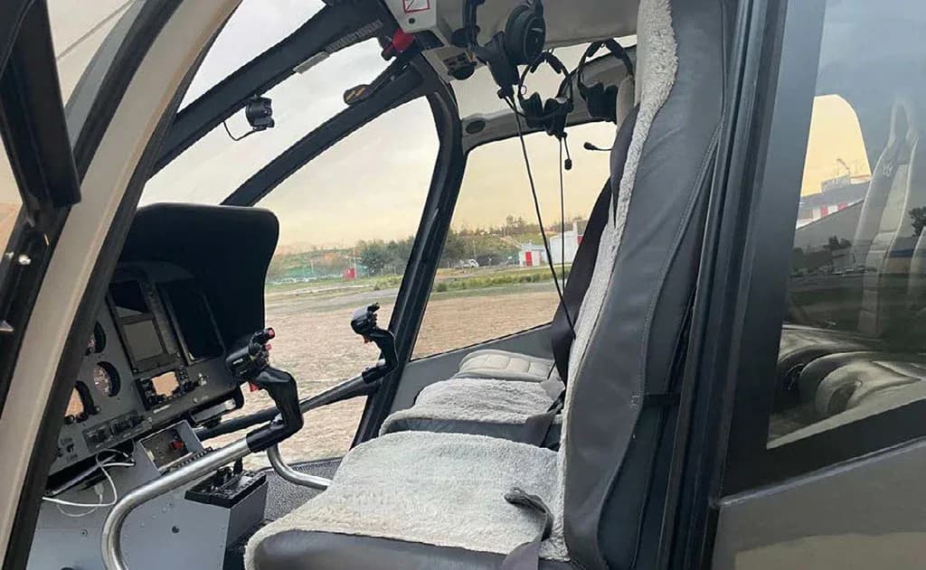 The helicopter cockpit shows the pilot's seat, controls, and a partial view of the instrument panel.