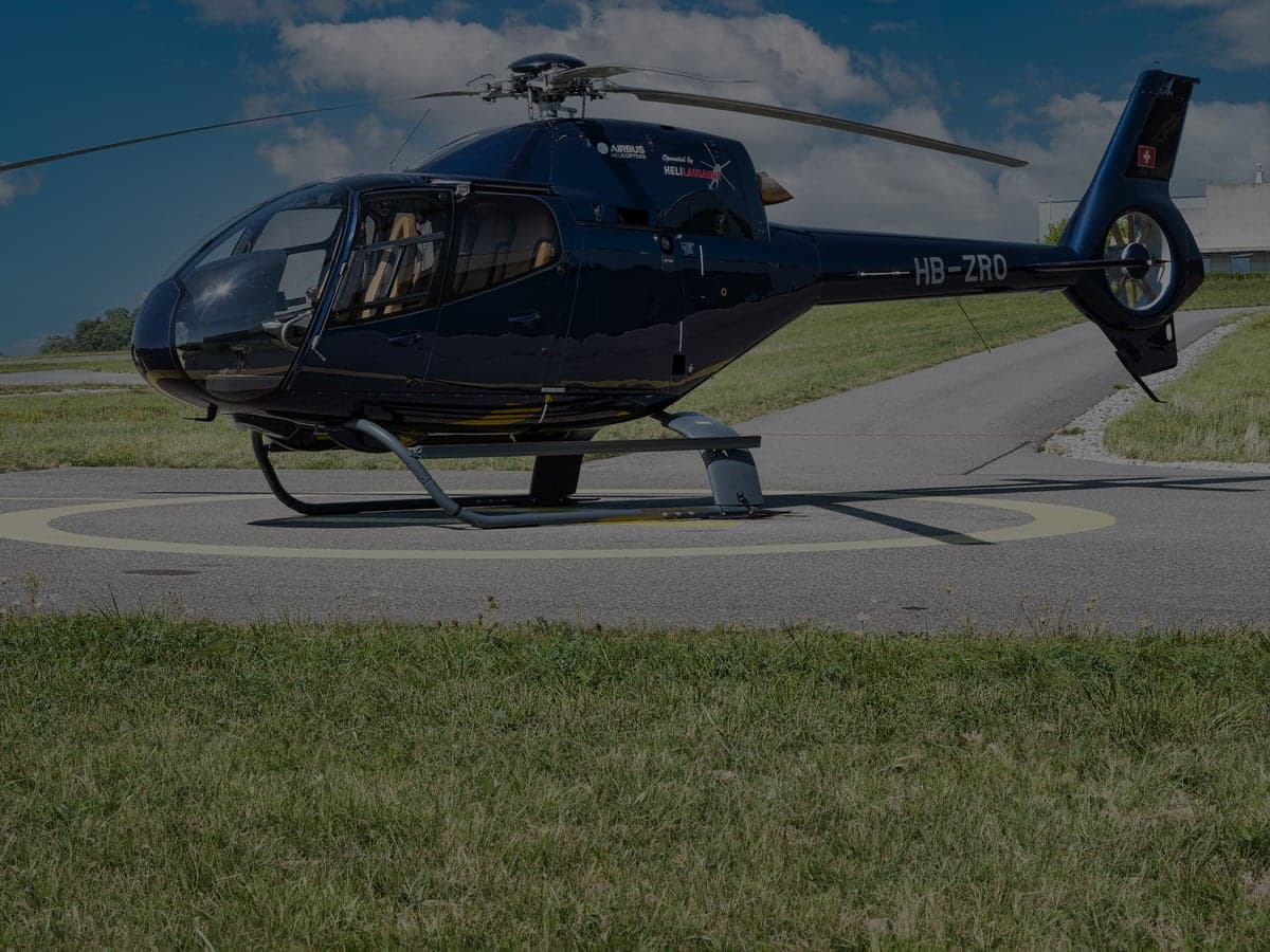 A dark blue Airbus helicopter is parked on a helipad.