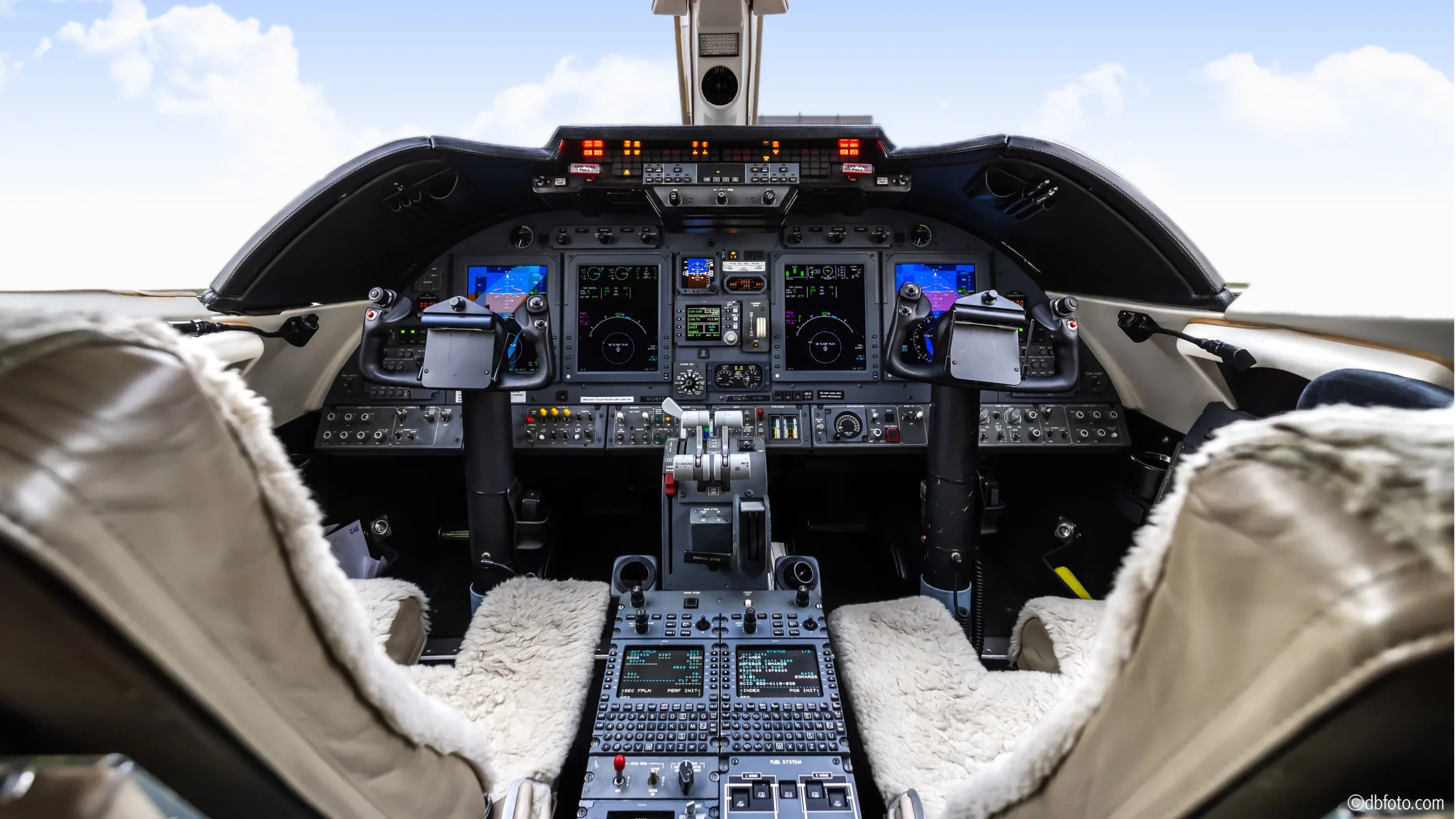 View of the aircraft cockpit with instrument panel and sheepskin seat covers.