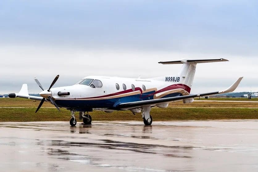 Pilatus PC-12 aircraft N998JB parked on the tarmac with a white, blue, and maroon paint scheme.