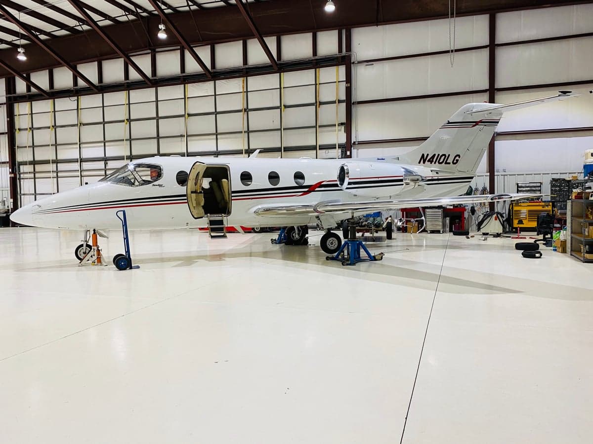 A white Learjet with red and black stripes and registration N410LG is parked inside a hangar with its door open.