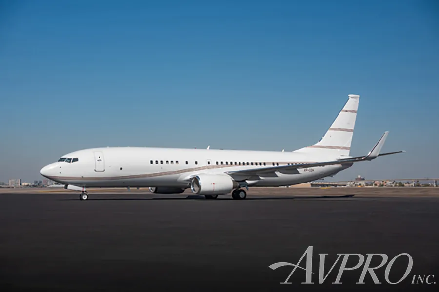 A white Boeing 737 business jet with brown stripes parked on a tarmac under a clear blue sky.