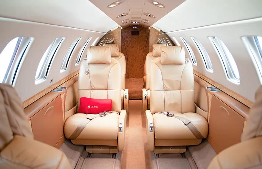 The luxurious cabin interior of a business jet with light tan leather seats facing each other.