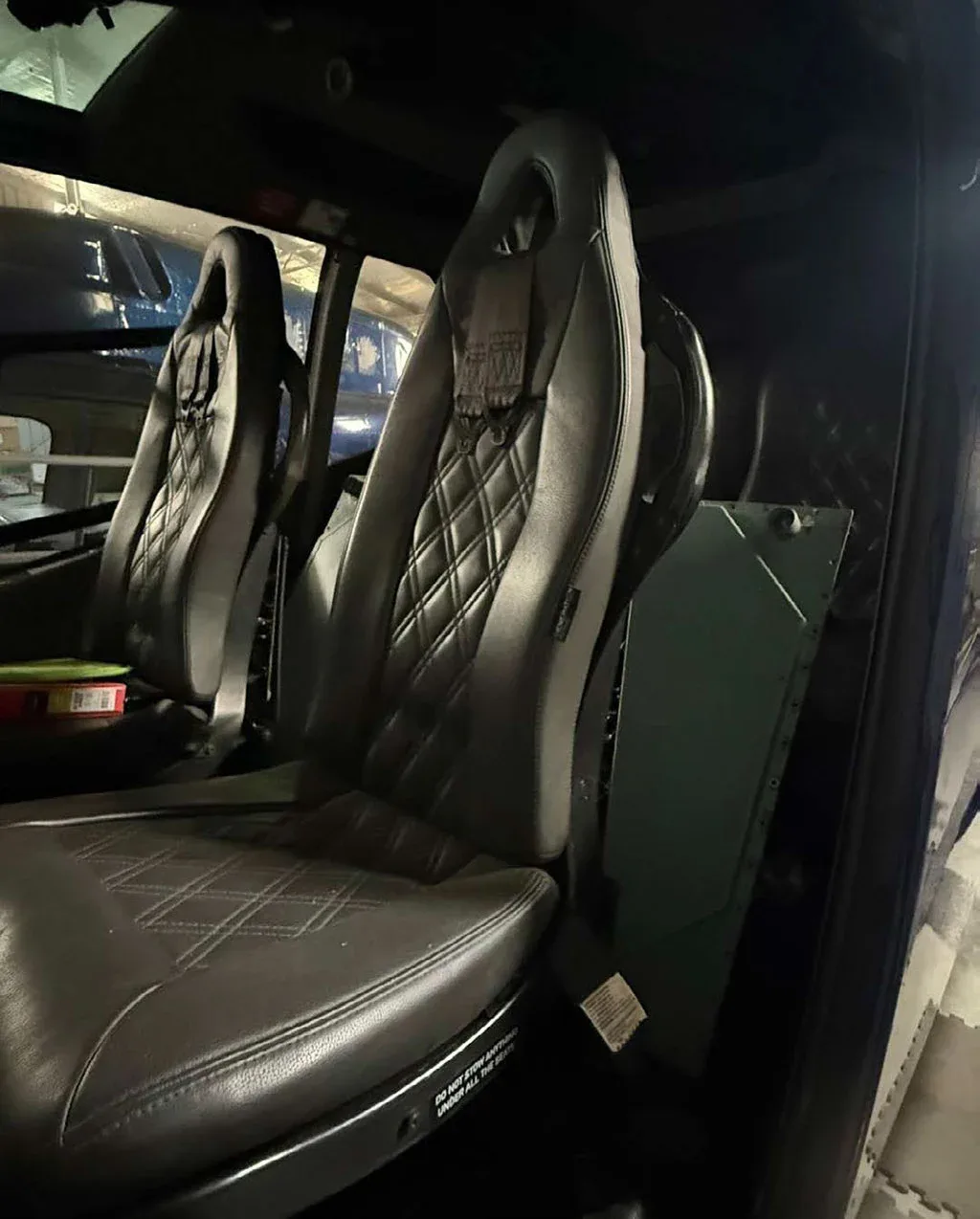 A close-up of the two black leather bucket seats with diamond stitching inside the helicopter cabin.