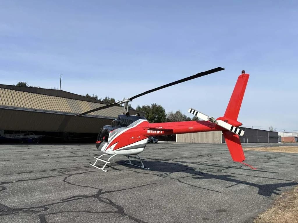 A red, black, and white helicopter with its tail rotor visible, parked on an airfield.