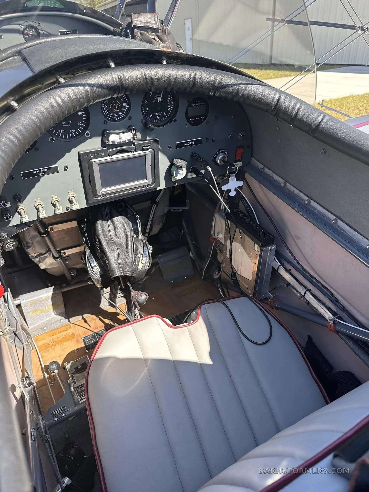 The rear cockpit of a gray biplane features a white seat, instrument panel with a GPS, and flight controls.