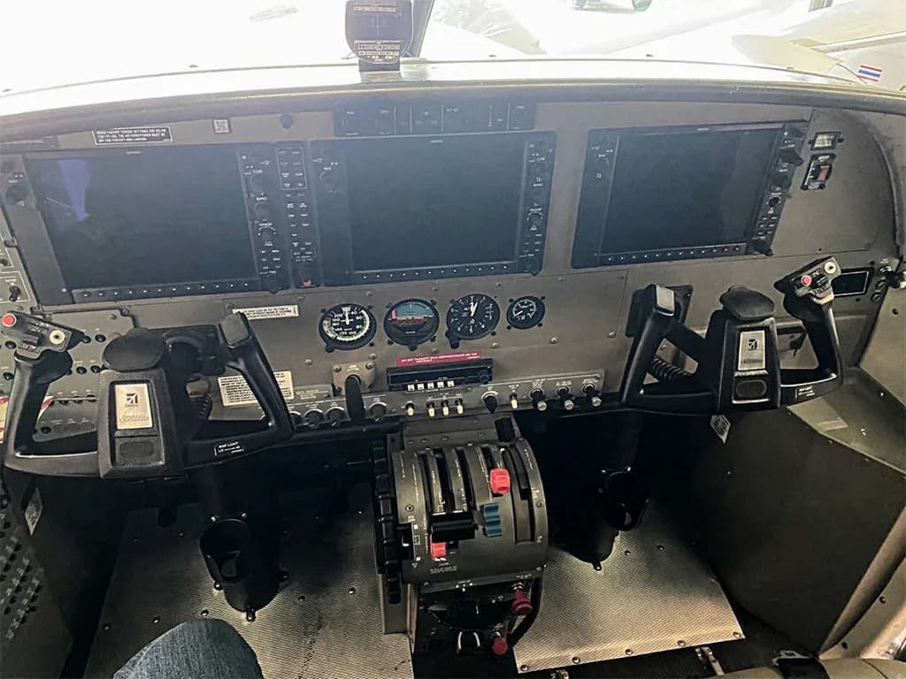 The cockpit of an aircraft features a modern glass panel with two large displays, analog gauges, and dual yokes.