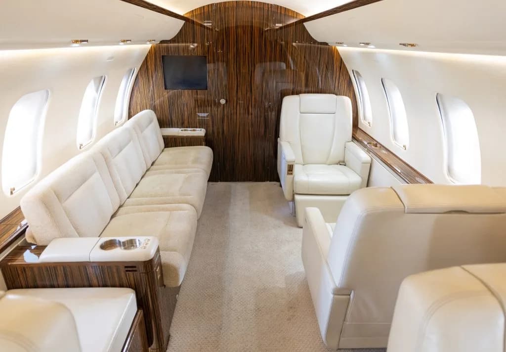 A wide view of the business jet's cabin, featuring a cream sofa and individual leather seats.