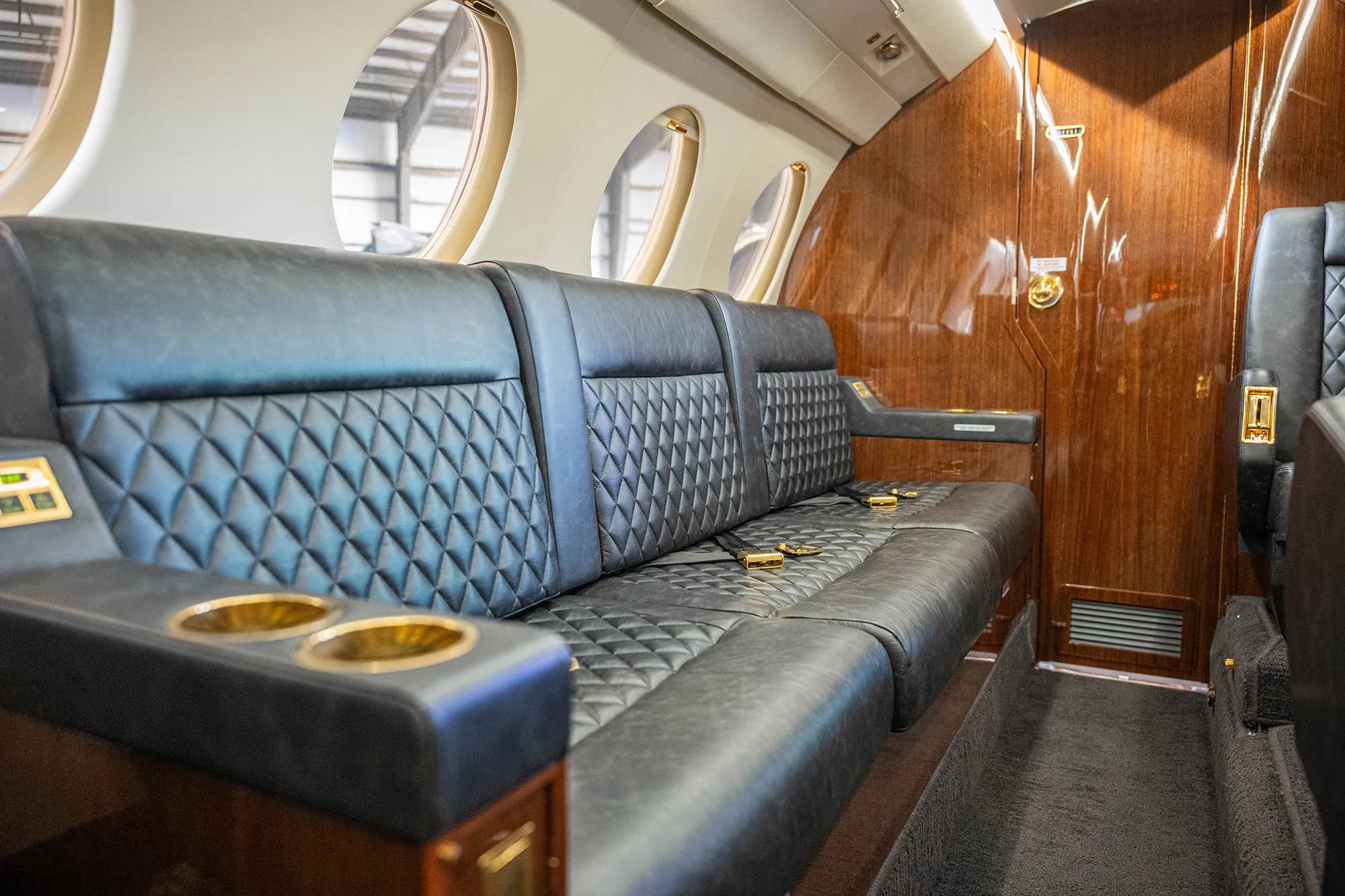 A close-up view of a dark quilted leather bench seat with cup holders in the cabin of a Dassault Falcon 900EX business jet.