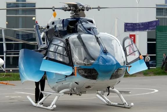 Front view of a blue and white helicopter with open doors on the tarmac.