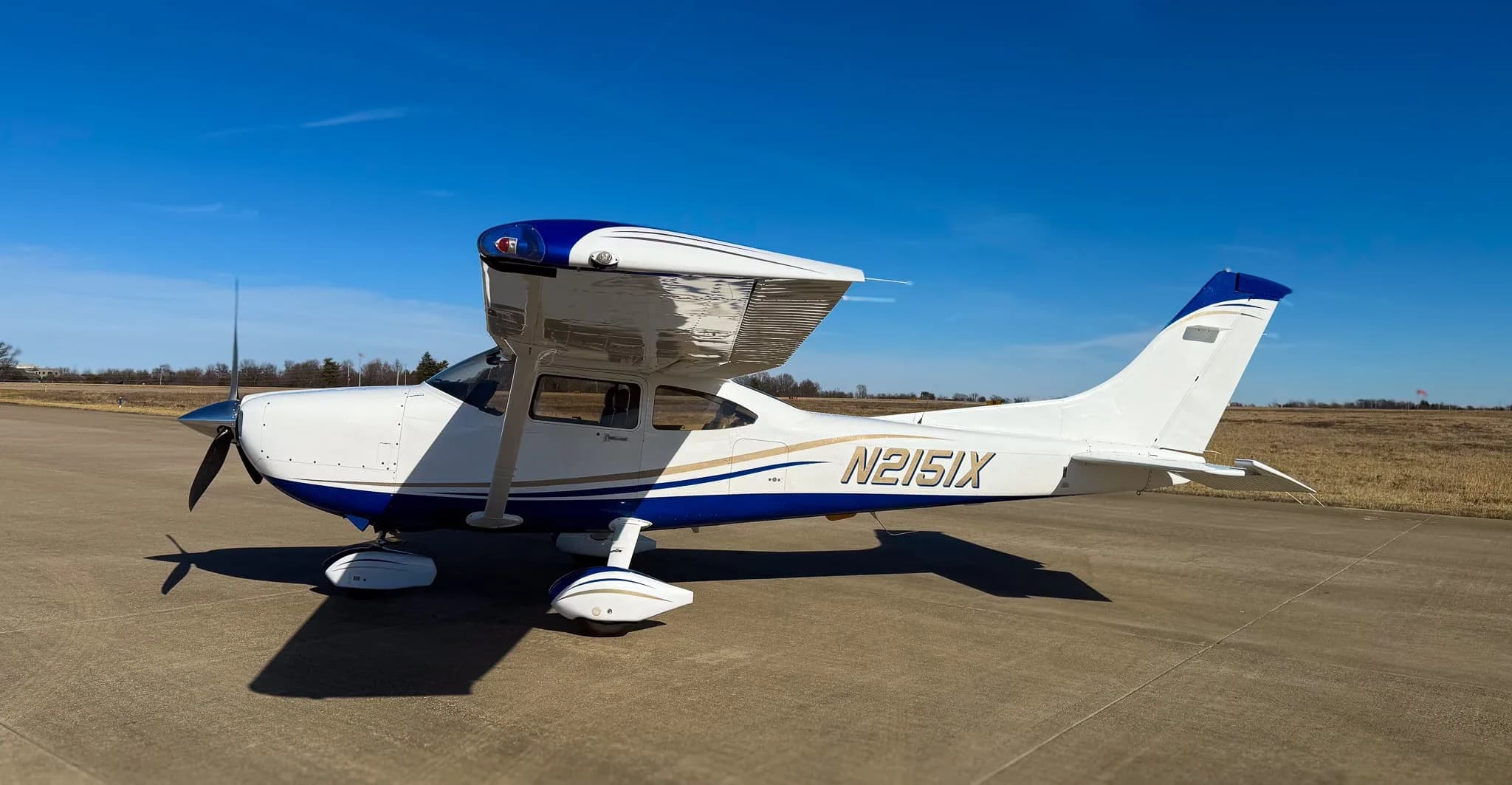 A white and blue Cessna 182 Skylane (N2151X) parked on a tarmac, viewed from the right side.