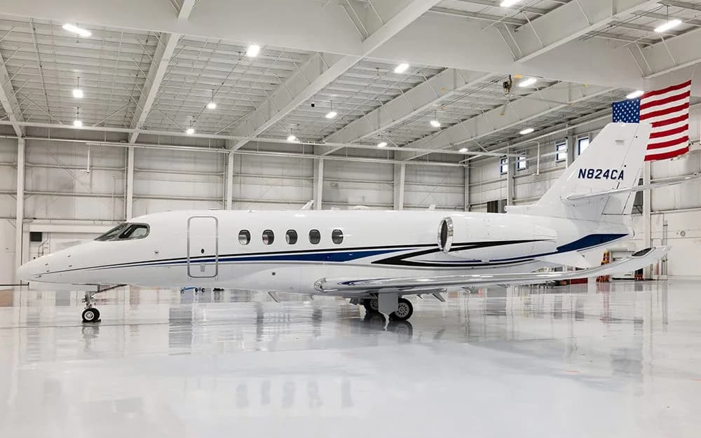 A white business jet with blue and black stripes, registration N824CA, parked in a brightly lit hangar with an American flag on the tail.