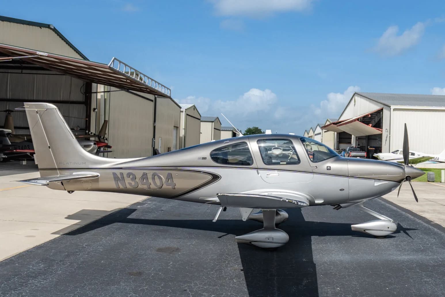 Side view of a silver Cirrus SR22T aircraft (N3404) parked on an airport tarmac under a blue sky.