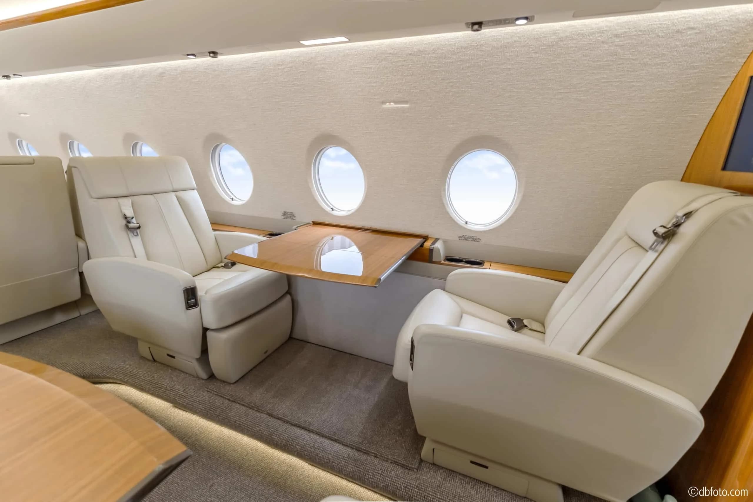 A close-up view of two cream leather seats with a polished wooden table extended between them.