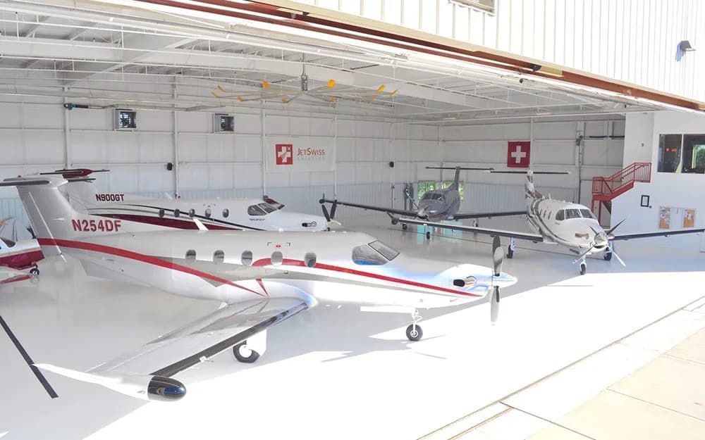 Three Pilatus PC-12 turboprops, one with red and white stripes and tail number N254DF, parked inside a bright white hangar.