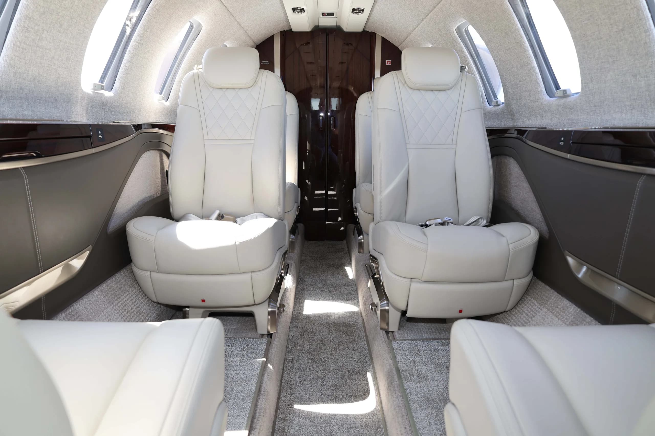 The interior cabin of a private jet, showing two rows of light-colored leather seats with quilted patterns.