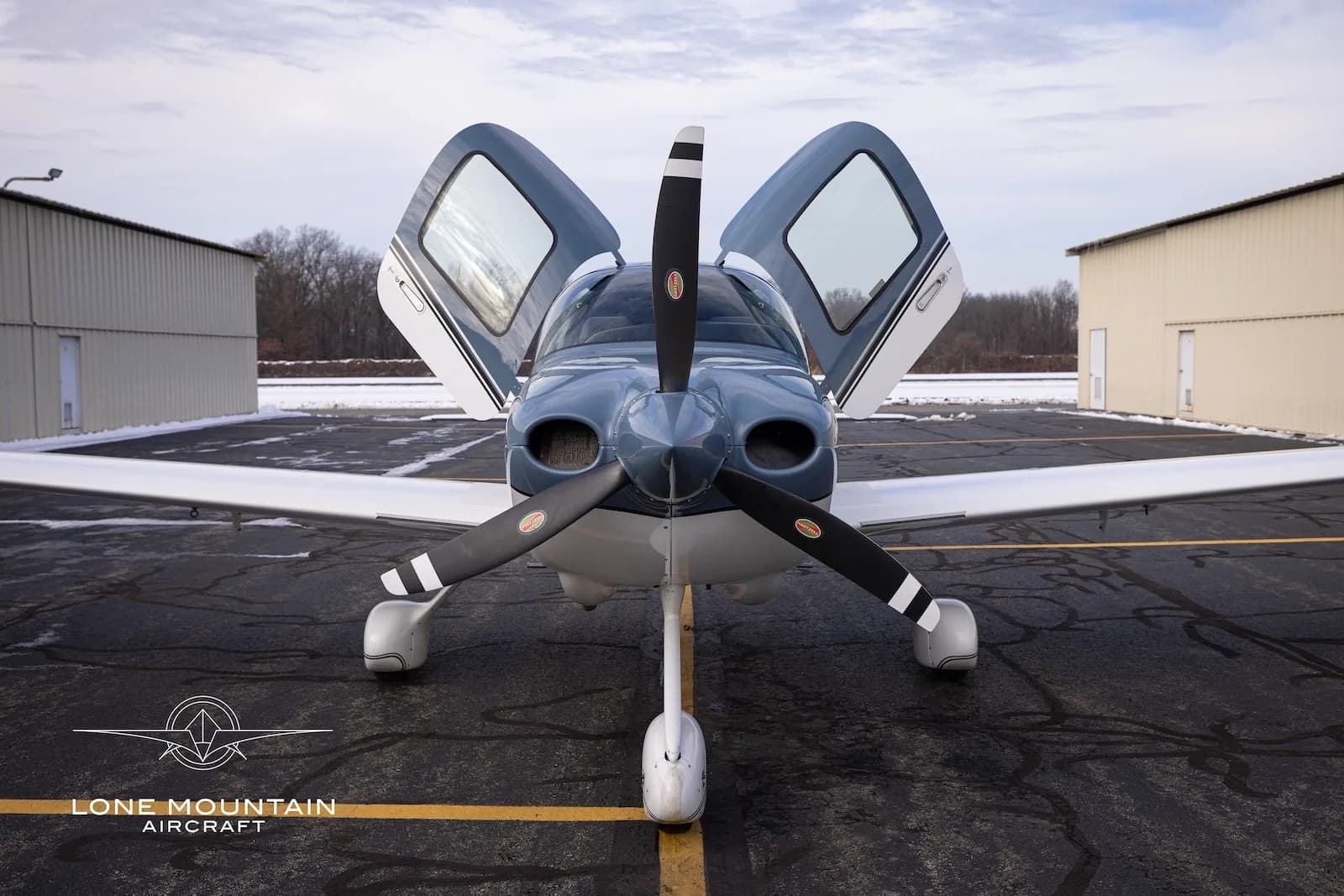 A front view of the Cirrus SR20 aircraft, N334MR, with its gull-wing doors open, parked on a tarmac.