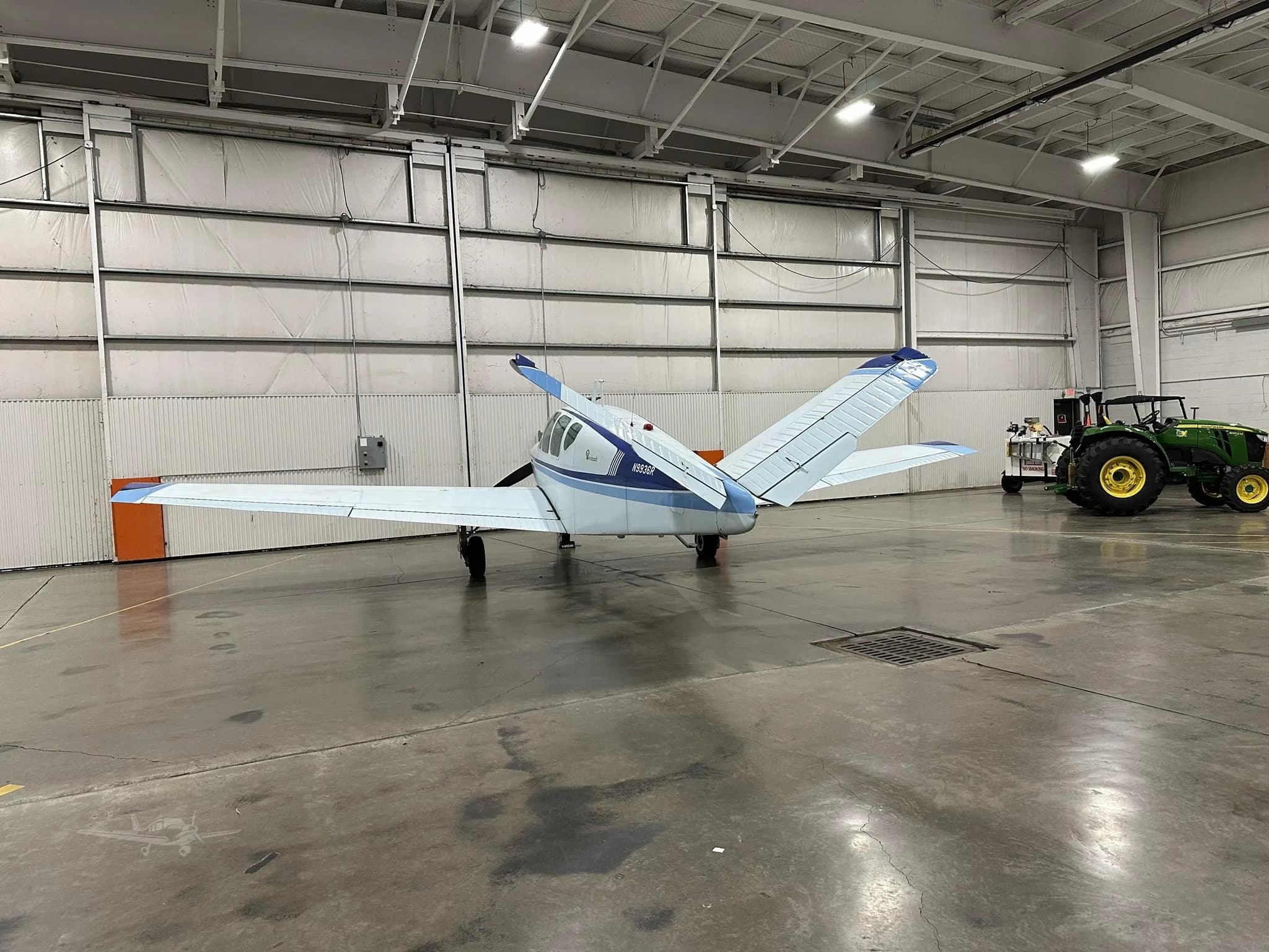 A white and blue Beechcraft Bonanza N9936R parked in a hangar, viewed from the rear.