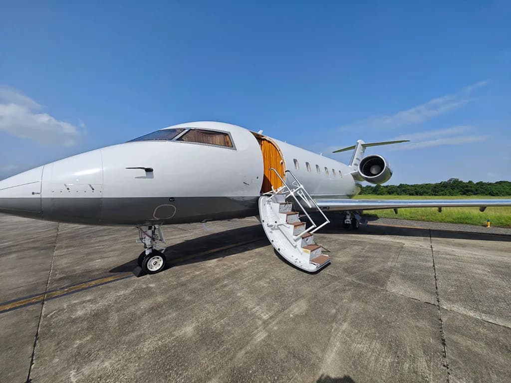 A front-side view of the white and grey Bombardier Challenger 604 business jet, N624EM, parked on an airfield with its main door open.