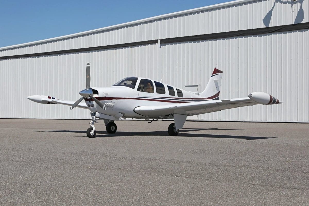 Side view of a white and red Beechcraft Bonanza aircraft parked in front of a hangar.