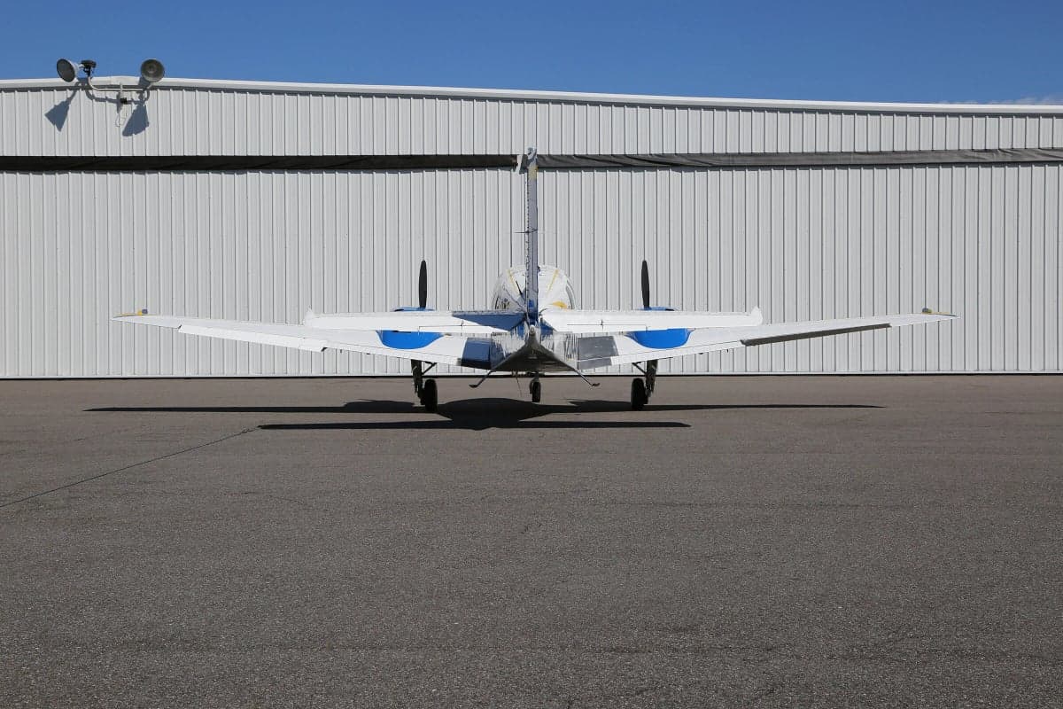 Rear view of a Piper PA-31 Navajo Chieftain aircraft parked on the tarmac in front of a hangar.