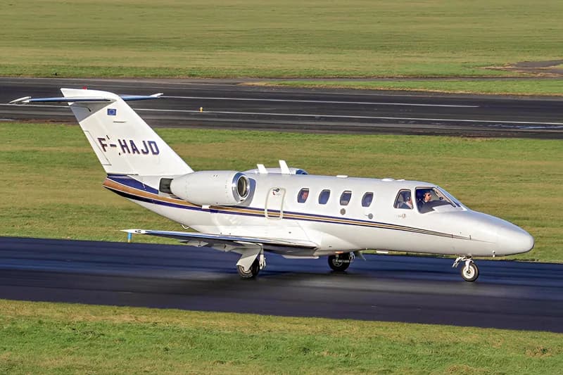 A white business jet with blue and gold stripes, registration F-HAJD, taxiing on a runway.