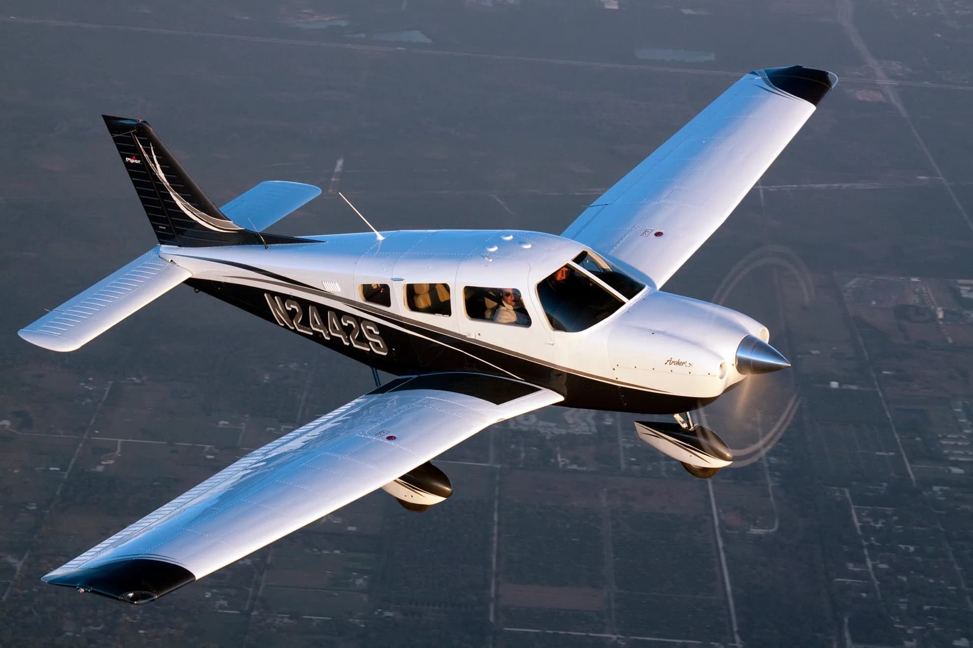 A white and black Piper Archer TX aircraft with registration N2442S is flying over a landscape, viewed from above.