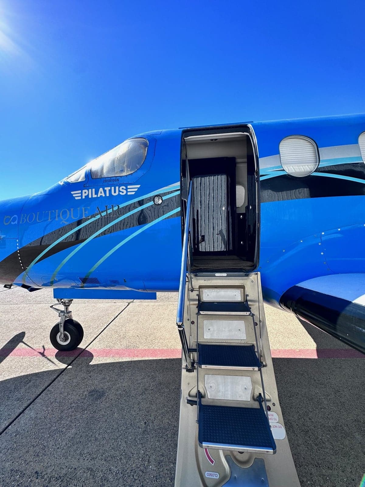 A blue Pilatus PC-12 aircraft with the door open and airstair extended on the ramp.