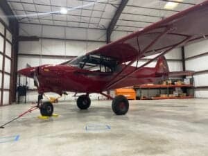 A red Cubcrafters aircraft is parked inside a hangar.