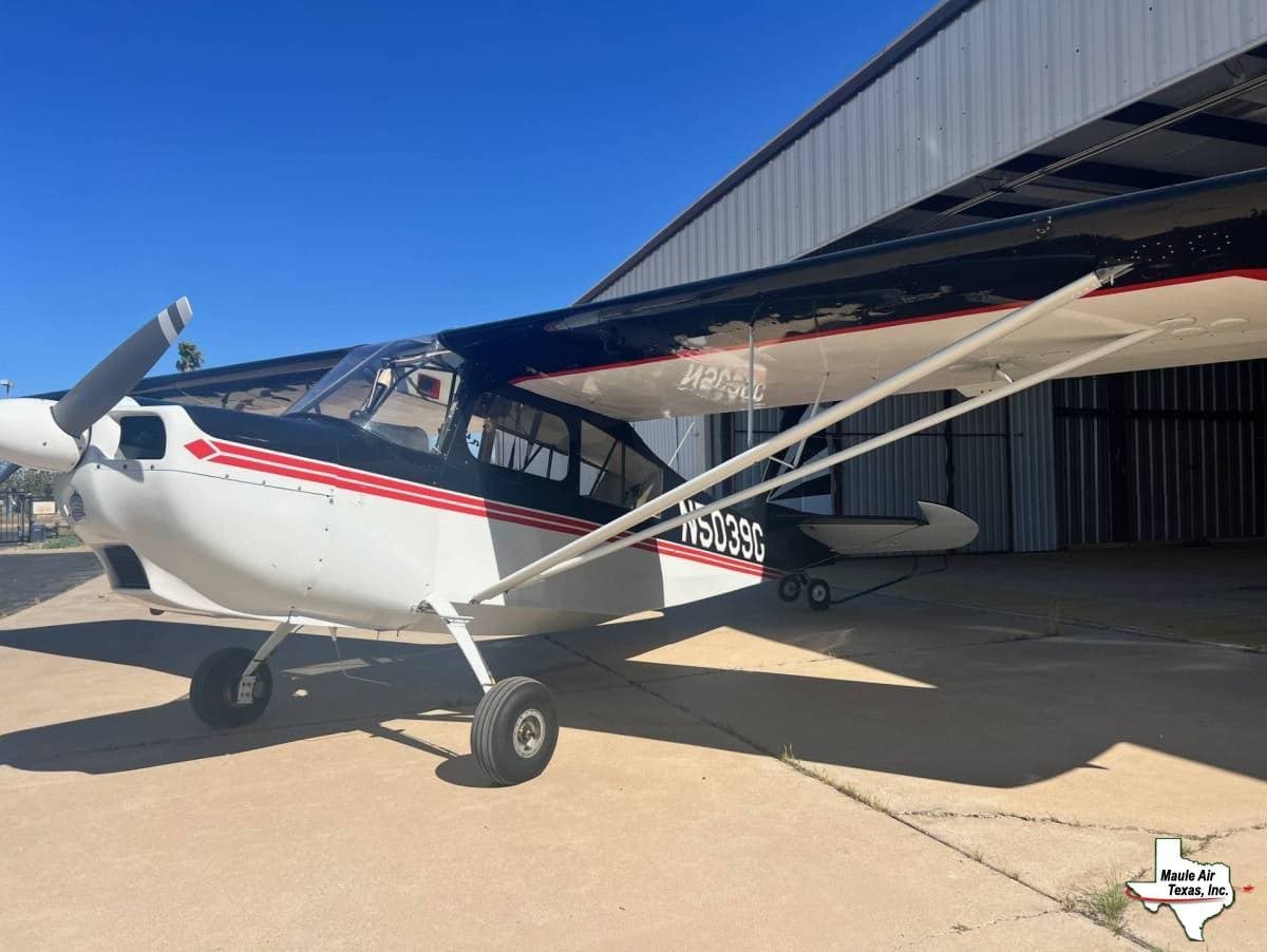 A white and black Maule aircraft with red stripes, registration N5039G, parked on concrete in front of a hangar.