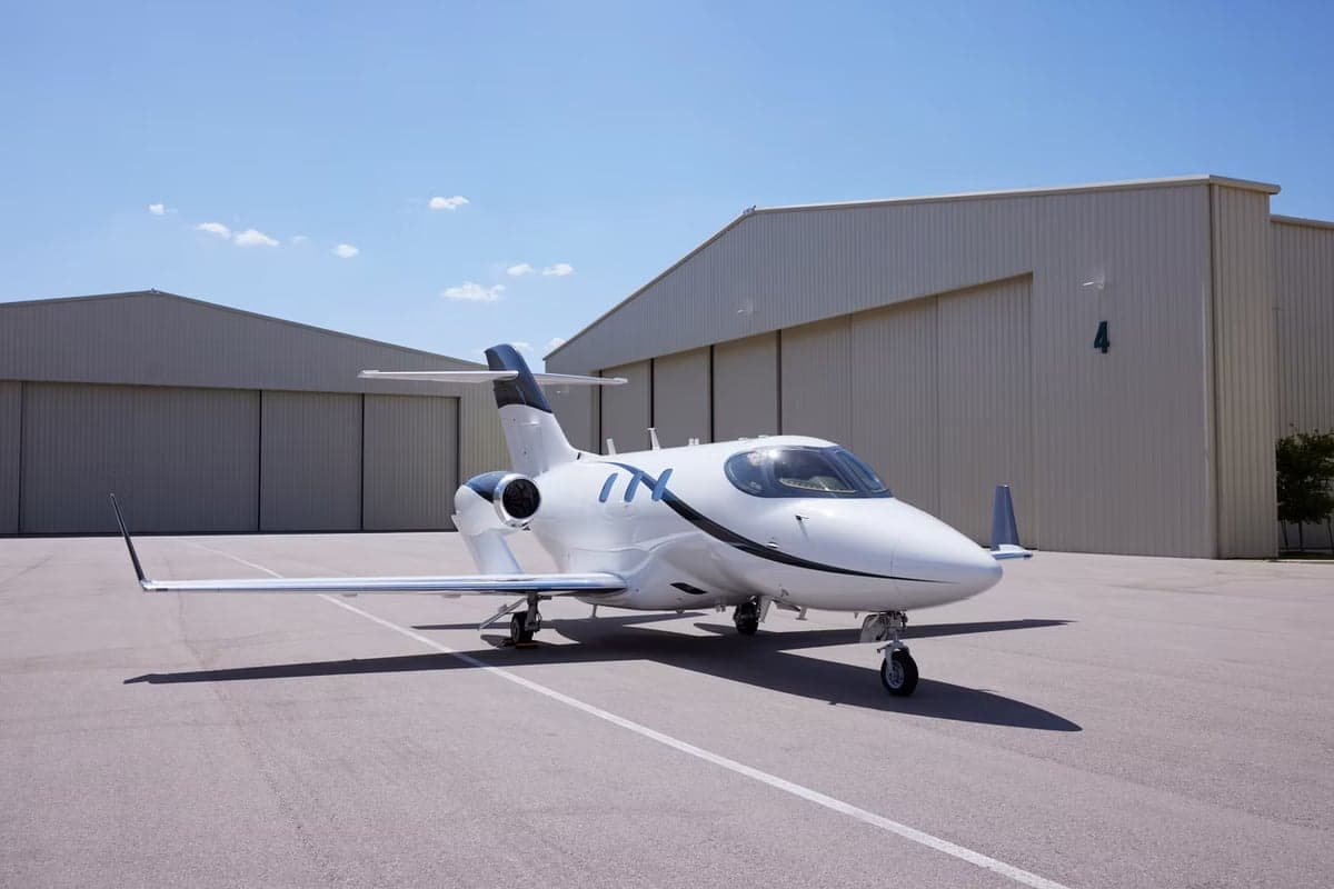 A HondaJet HA-420 is parked on the tarmac in front of a hangar.