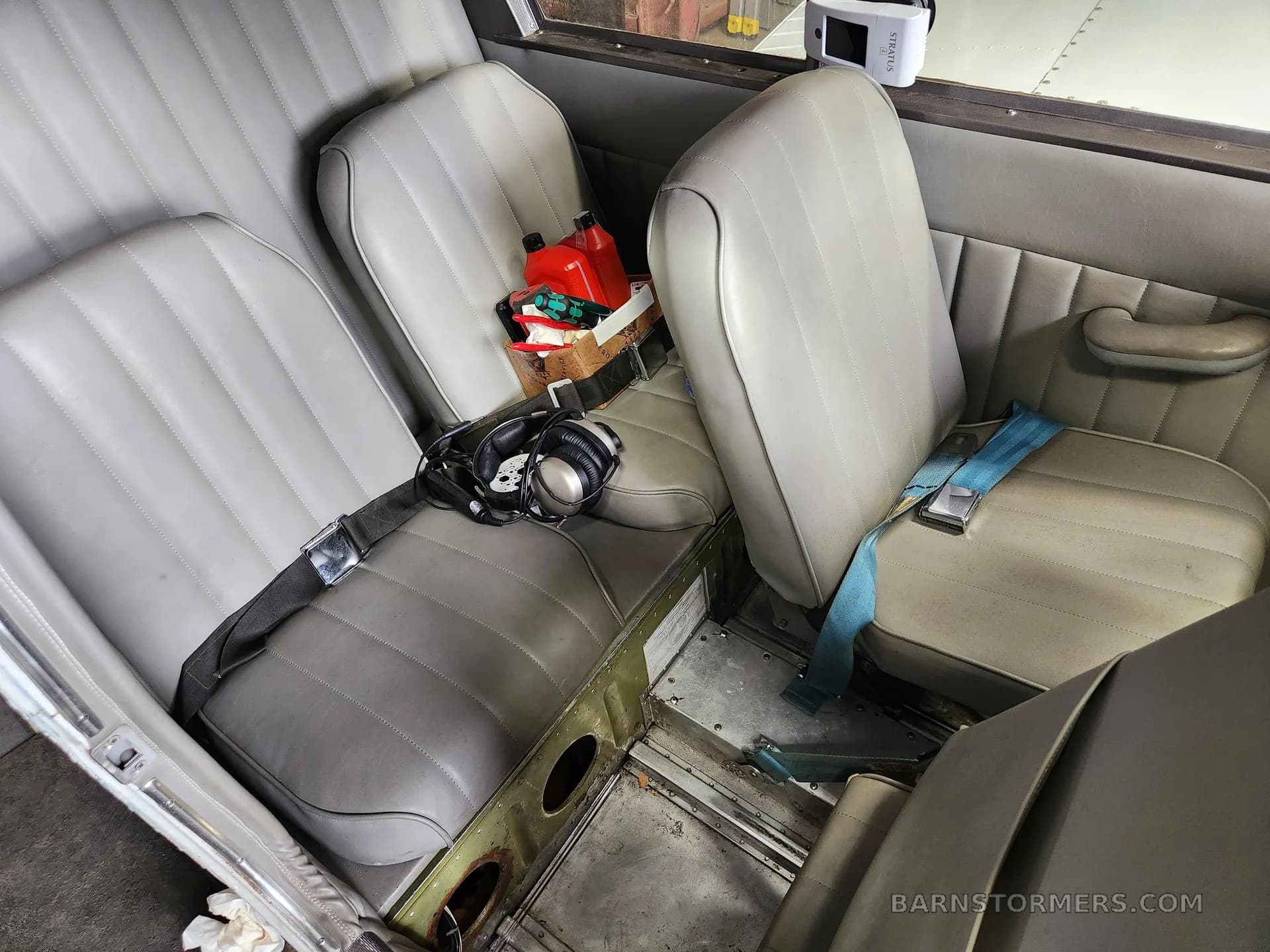 The light gray rear cabin seats of a Piper Cherokee aircraft, with a headset and a red fuel can on the seats.