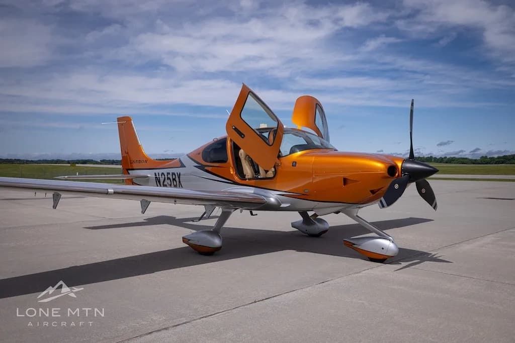 A front-right view of the orange and silver Cirrus SR22T N25BX with its doors open on an airfield.