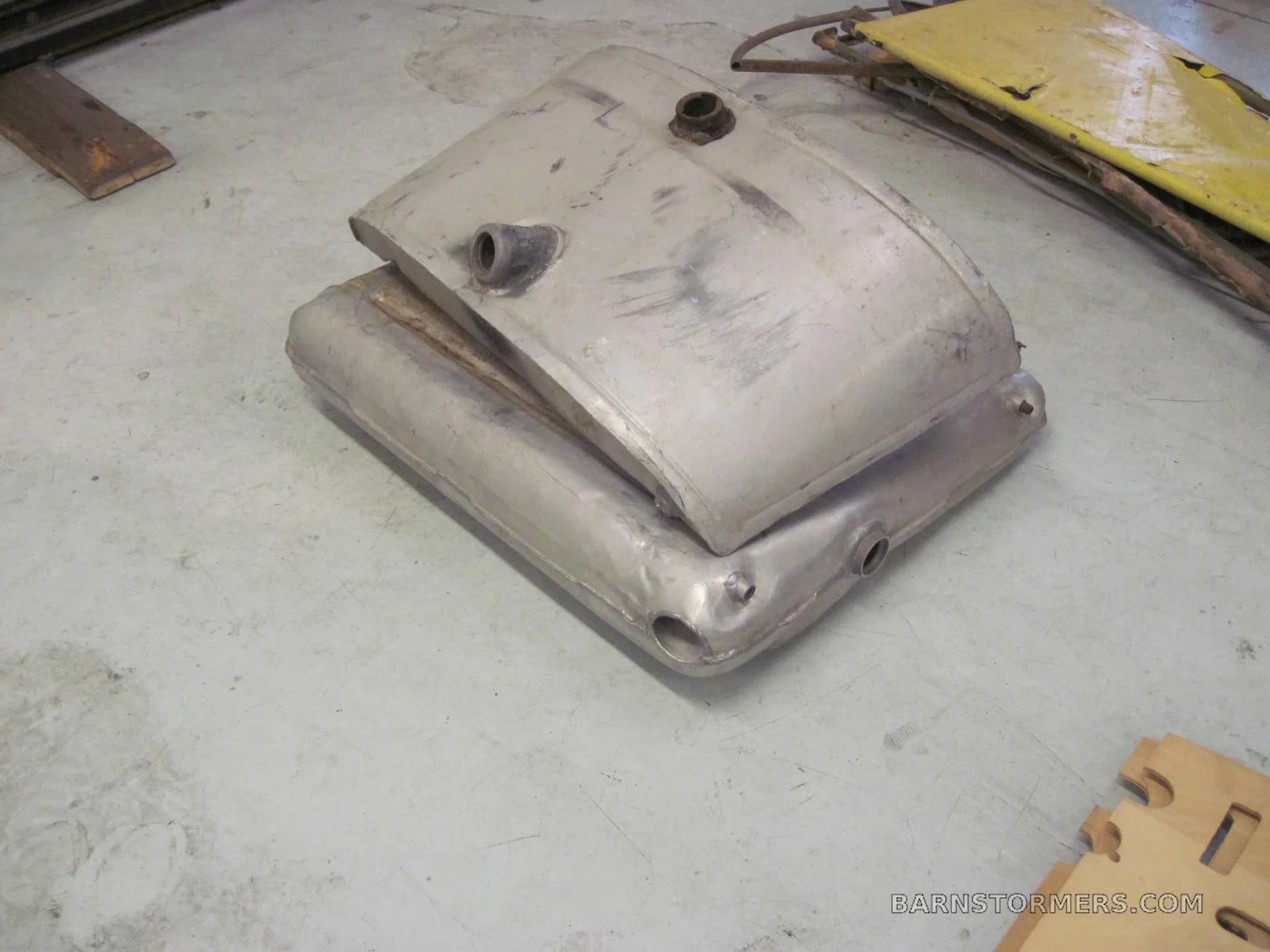 Two stacked, unpainted metal aircraft fuel tanks on a concrete floor.
