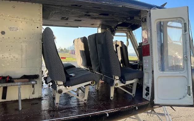 The helicopter's cabin interior showing several black fabric seats and an open side door.
