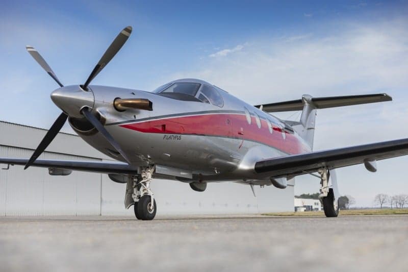 Close up of a Pilatus PC-12 aircraft with a silver and red paint scheme parked on the tarmac.