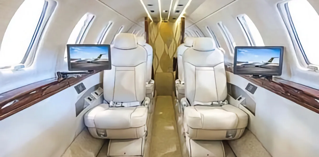 Aircraft interior with white leather seats and entertainment screens.