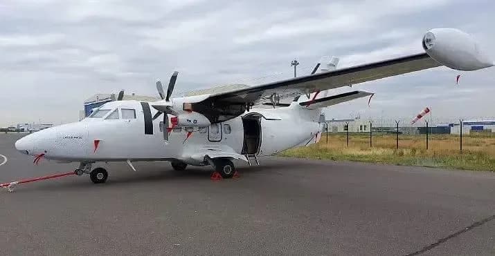 A white aircraft is parked on the tarmac with the door open.
