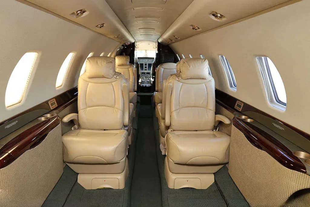 The interior cabin of a private jet with beige leather seats, looking forward towards the cockpit.