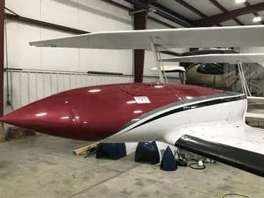 The nose of the maroon and white Cessna 340A aircraft is shown inside a hangar.