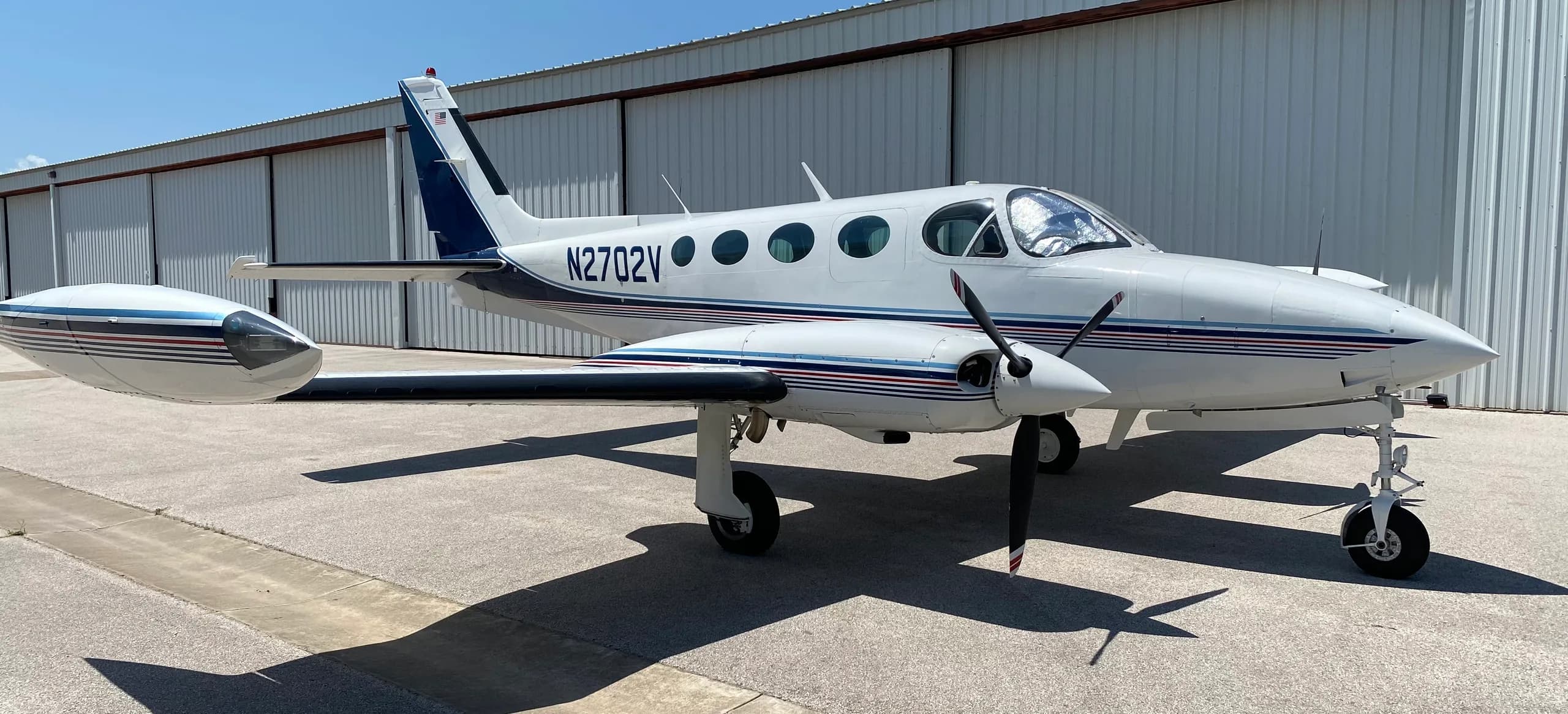 A Cessna 340A aircraft with registration N2702V parked in front of a hangar, front quarter view.