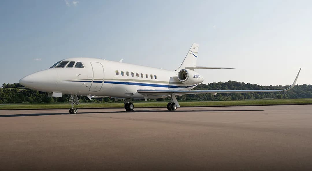 A Falcon aircraft is parked on the tarmac with a white paint scheme and blue accents.