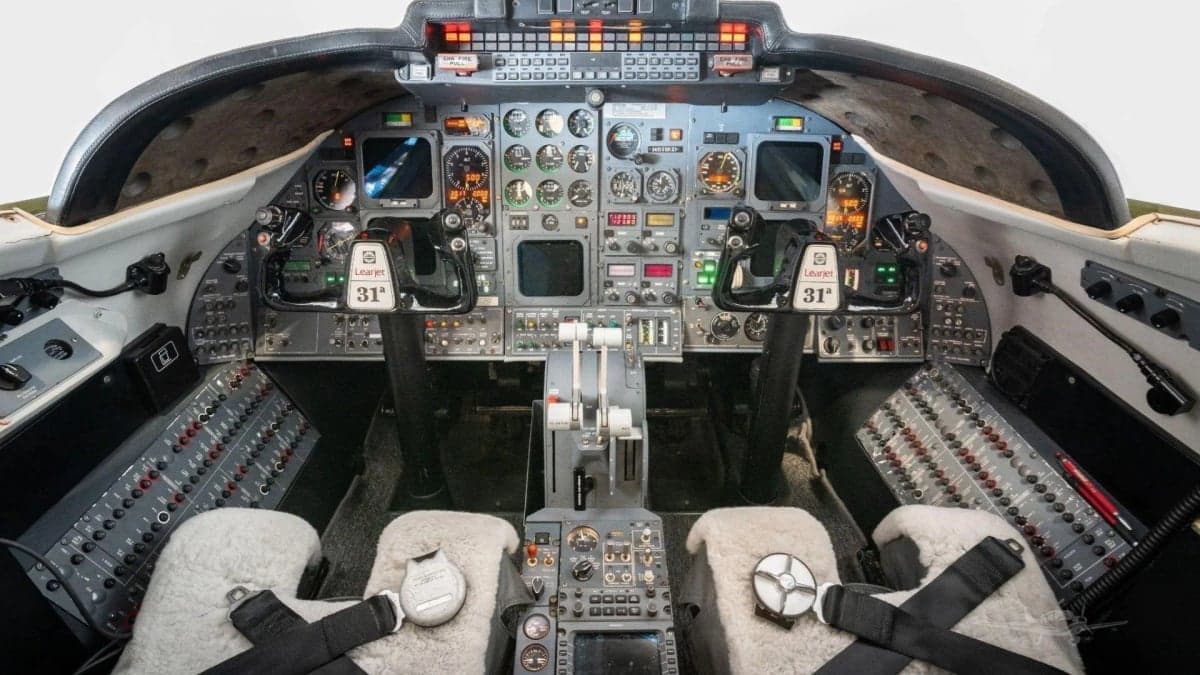 Wide view of a Learjet 31A cockpit with two sheepskin-covered seats, control yokes, and a full instrument panel.