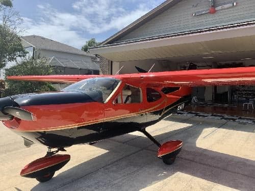 A Cessna Cardinal RG with a red and black paint scheme is parked outside a hangar.