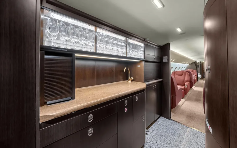 A well-equipped aircraft galley with dark wood cabinetry, a sink, and illuminated glass storage for stemware.