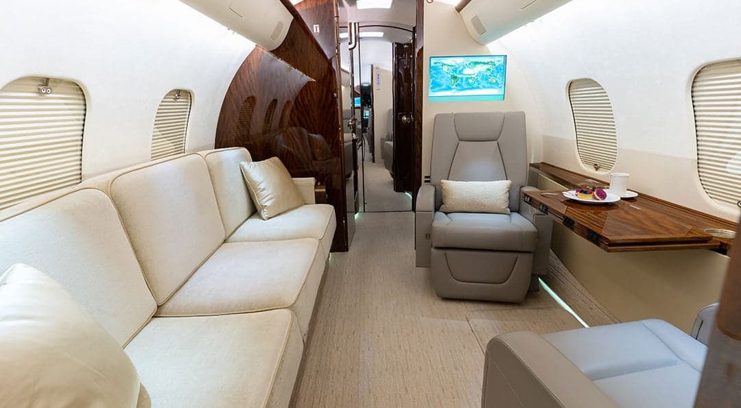 A view of the aircraft's interior, showing a sofa, leather seats, wood trim, and a table set with food and drinks.