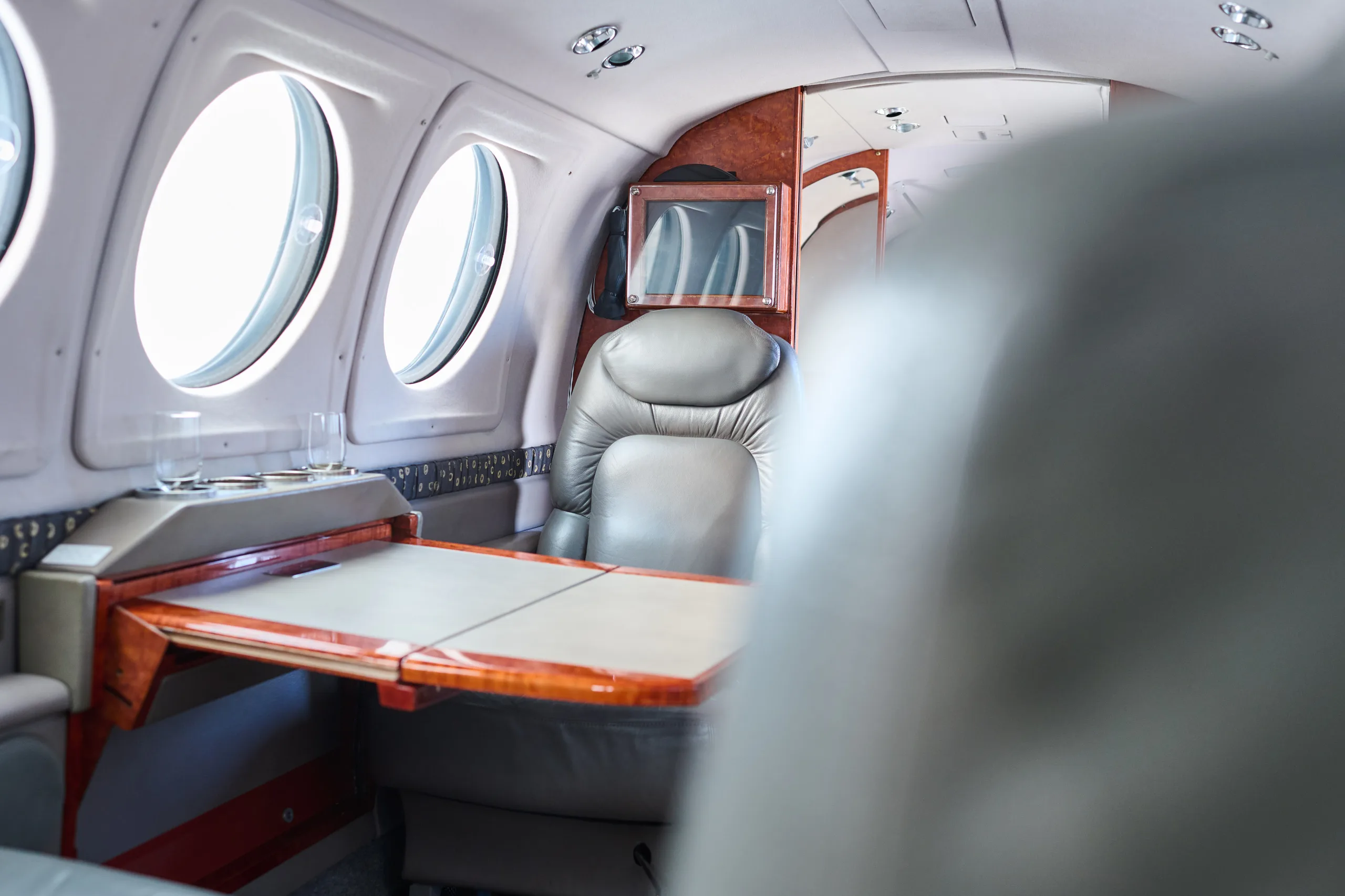 A view inside the aircraft cabin highlights a wooden table with drink holders and a grey leather seat.